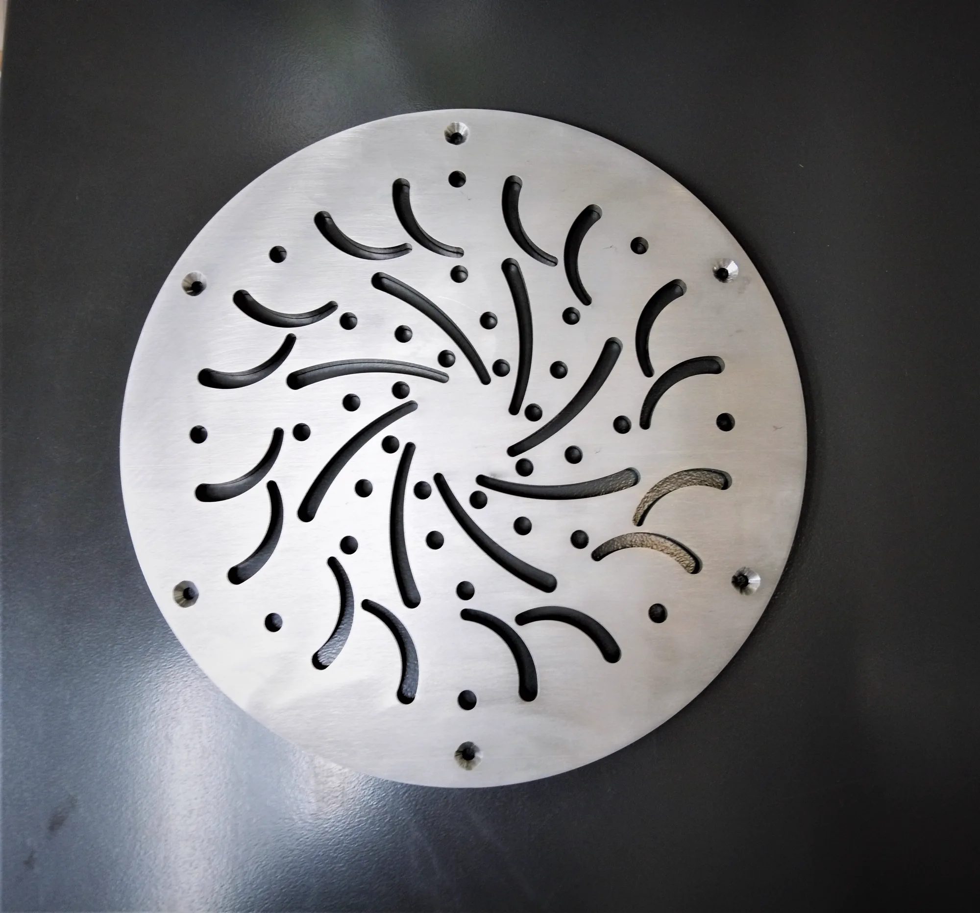 Round metal plate with precision laser-cut curved slots and holes